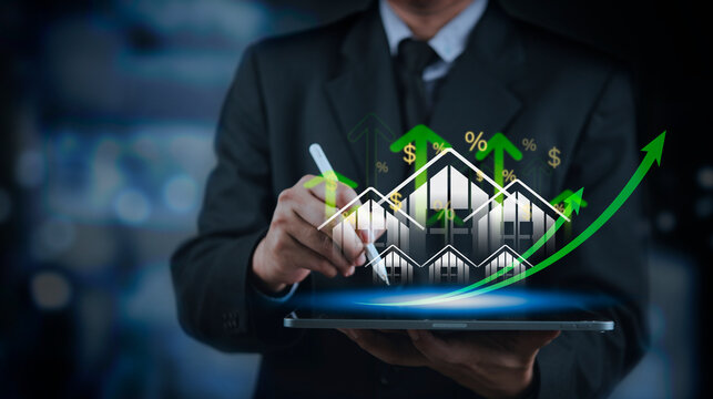 Businessman using tablet with glowing houses green arrows and percentage signs. Concept of real estate investment property value growth housing  mortgage interest rate and profit.