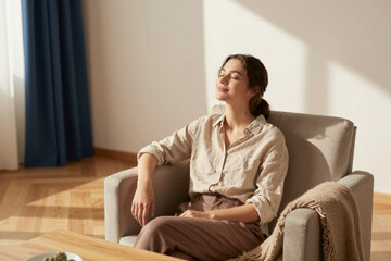 Fototapeta premium Woman enjoying sunlight while seated in living room apartment