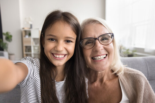 Close up webcam faces, older 55s grandma and 7s grandkid, gazing at camera, make selfie or videocall, record video vlog, looking with joyful expression. Hobby, fun, leisure of multigenerational family
