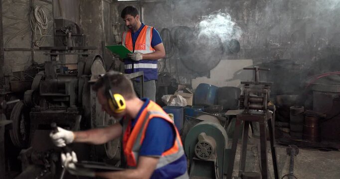 Factory technicians inspect machinery and discuss repair steps in a metal workshop, showing teamwork, maintenance coordination, safety, and industrial support.
