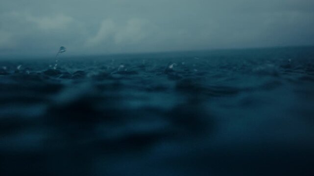 Dark ocean surface during heavy rain with raindrops splashing across choppy water, abstract storm texture bouncing water