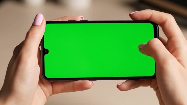 A person holding a smartphone horizontally with a green screen for chroma key compositing.