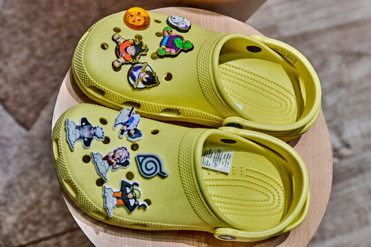 Ambato, Ecuador - June 09, 2025: Yellow Crocs with colorful Dragon Ball character charms displayed on a wooden pedestal in a vibrant Crocs store at Mall de los Andes