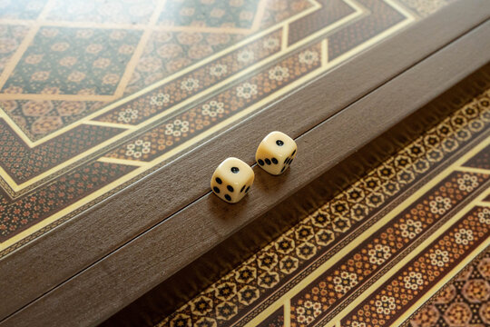 Dice On Patterned Backgammon Board, Two Dice Aligned Along Playing Track, Muted Warm Tones, Fine Geometric Inlay, Tactile Wood Grain, Sense