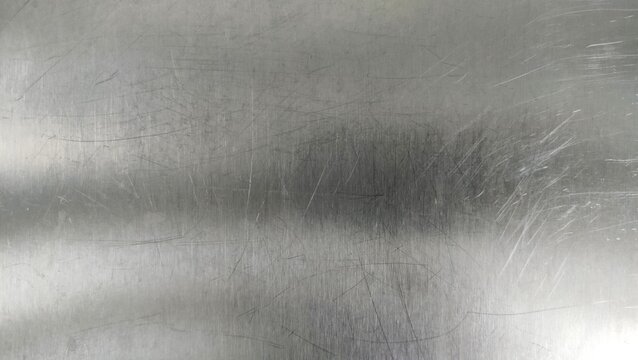 close-up of a scratched metal surface, possibly stainless steel or aluminum. The texture is rough, with numerous fine and deep scratches crisscrossing in various directions, creating a worn and aged