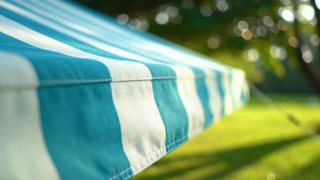 A close-up view showcases a blue and white striped awning extending over a blurred green background, suggesting a pleasant outdoor setting.