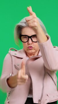 Stylish senior woman making a gun gesture on a green screen