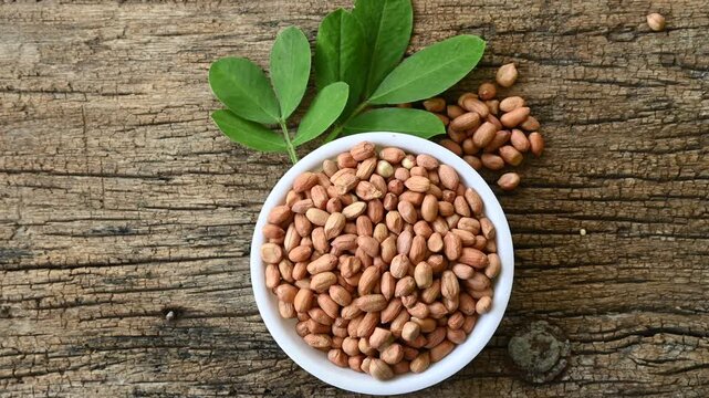 Raw peanuts in white bowl with green leaves on rustic wooden background