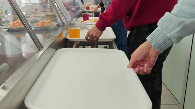 A person carrying a white tray with a fresh vegetable salad and a fork in a cafeteria or dining hall setting.