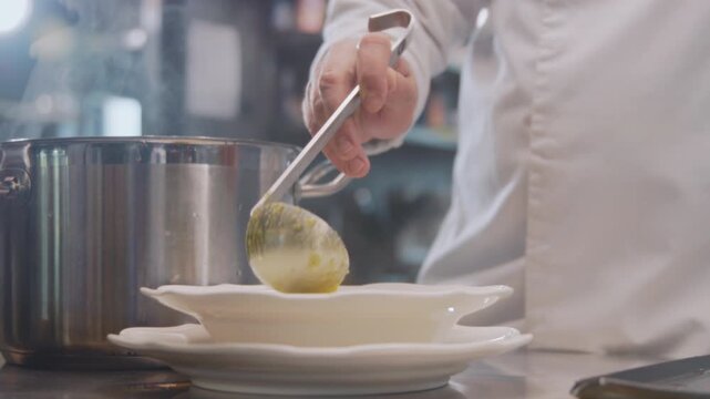 Steaming liquid being poured into bowls swiftly, Culinary staff carefully filling porcelain dishes with thick soup