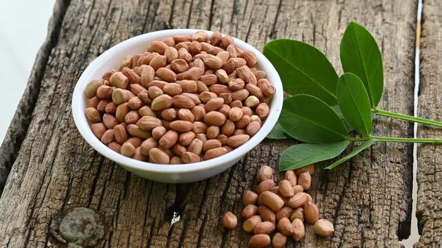 Raw peanuts in white bowl with green leaves on rustic wooden background