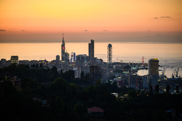 Naklejka premium Seaside Evening Glow. Evening Falls On Lively Harbor. Black Sea Shoreline Transforms Under Enchanting Twilight Illumination. Sunset Bathes Busy Coast In Warm Hues As Night Approaches Black Sea