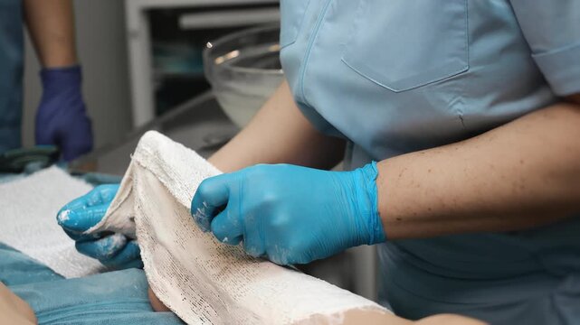 Doctor preparing plaster cast bandage in clinic for child leg immobilization orthopedic treatment process trauma care and injury recovery concept indoors.