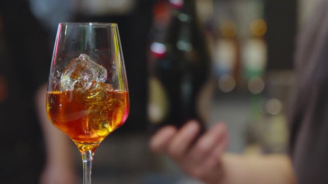 Bartender pouring sparkling wine into a glass with orange drink