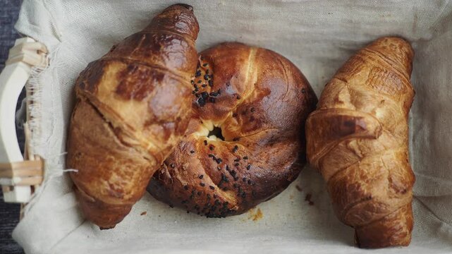 Freshly baked croissants and pastry with black seeds in basket on rustic wooden table.