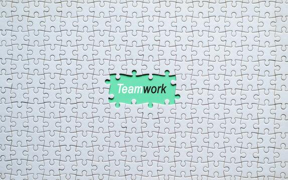 White jigsaw puzzle with missing pieces showing teamwork word on green background