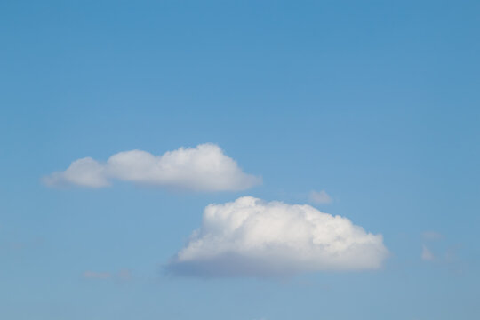 Two fluffy white cumulus clouds floating in a clear blue summer sky