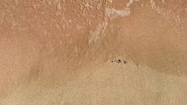 Waves wash over sandy beach, erasing the word summer written in the sand, showcasing the dynamic interaction between water and shore in a coastal environment