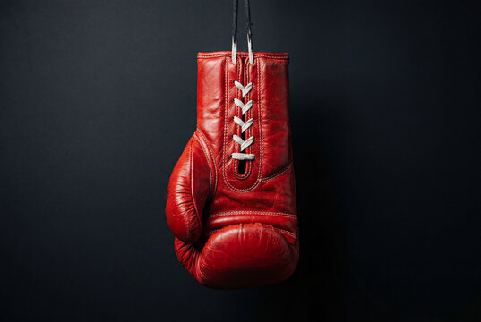 Red leather boxing glove hanging against dark black background
