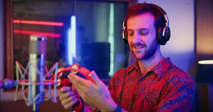 Microphone, tambourine and musician in music booth with headphones for recording song with talent. Singer, instrument and male artist singing with audio tech for production on album in sound studio.