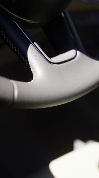 A close up captures the sleek design of a modern car steering wheel, showcasing the texture and finish. The interior features a minimalist style with ambient light streaming through.