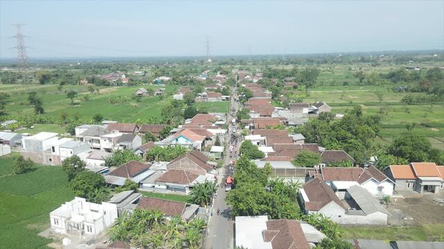 Aerial 4K view of a rural village settlement surrounded by vast green rice fields and farmlands.