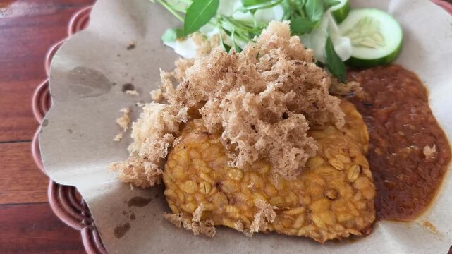 Traditional Indonesian tempeh dish served with spicy sambal, fresh vegetables, crackers, and cucumber slices