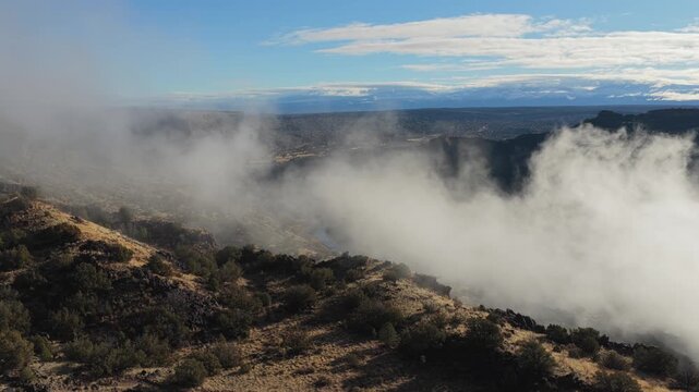 Dramatic white mist is shown forming and drifting through a deep rocky canyon landscape. The footage captures the atmospheric weather patterns as clouds develop within the rugged wilderness gorge.