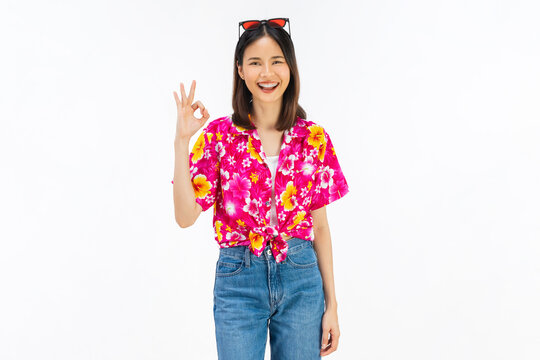 Smiling young Asian woman showing OK hand gesture in summer floral shirt isolated on white studio background.