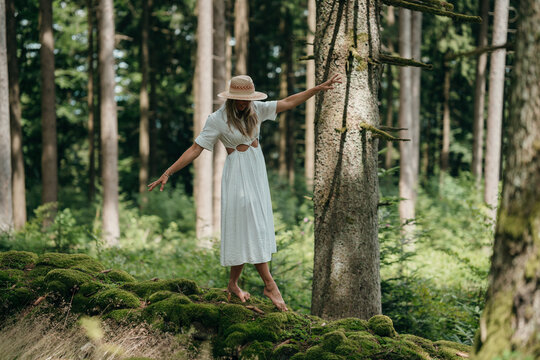 A woman walks peacefully on a mossy stone wall in the forest enjoying nature and escaping the stress of everyday life in calm solitude