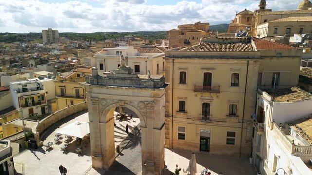 Aerial view of Porta Reale in Noto, showcasing the historic arch and surrounding architecture in a vibrant cityscape filled with rooftops and greenery