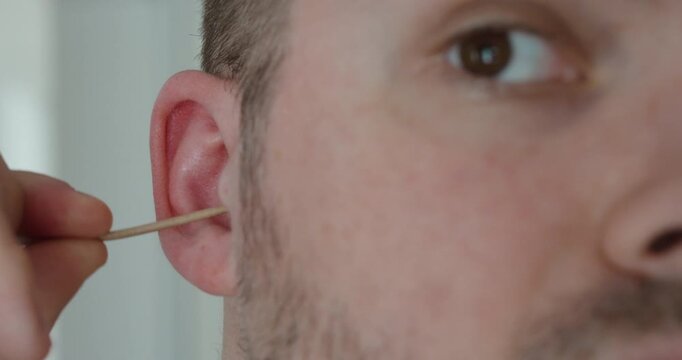 Close-up of a man cleaning the outer ear with a cotton swab. Concept of hygiene, personal care and ear cleaning safety.
