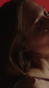 Beautiful vertical close up of a sensual woman undoing her white brassiere in slow motion while posing in a dark room