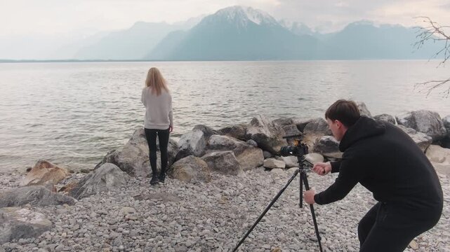 Male photographer posing a blonde model with lake at beach during the day, gimbal shot