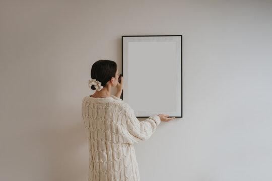 Back view woman adjusting framed poster mockup on wall in modern home decor scene