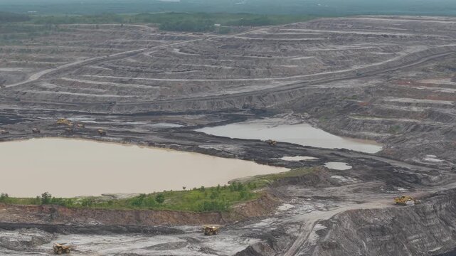 Aerial view of excavator and coal hauling truck activity, near a very deep excavation pit