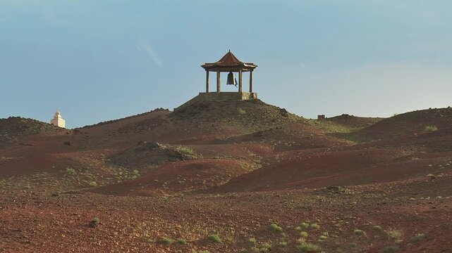  Mongolia, the Gobi Desert. A small Buddhist chapel with a bell among the harsh Martian landscape with volcanic stones and sparse vegetation. It's raining.