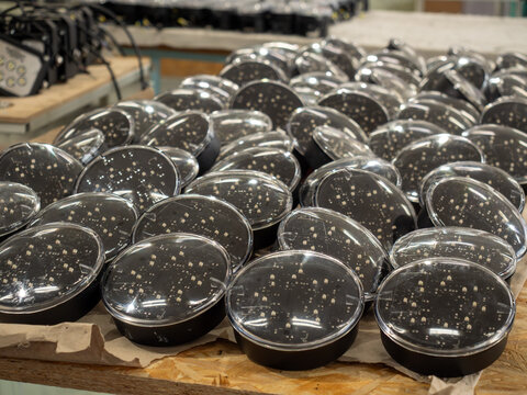 Rows of circular black searchlights with transparent protective covers displaying internal LED chips arranged on workbench during manufacturing process within industrial electronic assembly plant.