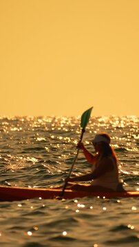 Kayaking sunset ocean woman paddling orange kayak sparkling golden water adventure lifestyle Vertical video