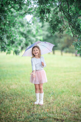 Little girl smiling and laughing under an umbrella while standing near a large tree in the rain. Free play and positive energy in the middle of a wet outdoor day. © dtatiana