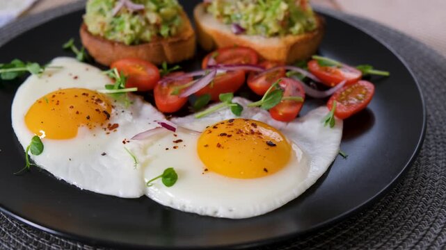 Rotating healthy breakfast with avocado toast and fried eggs on dark background