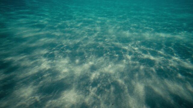 Underwater over sandy seabed with rippled patterns and clear blue water, soothing calm empty reflections of dancing light rays