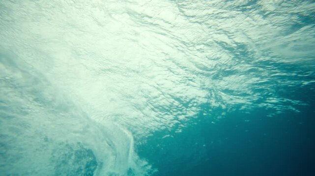 Underwater of surfer passing above with board and white foam tail chasing, slow motion
