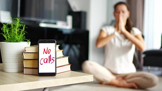 Digital detox concept. In the foreground is a smartphone with the text No Calls and woman meditating in the background