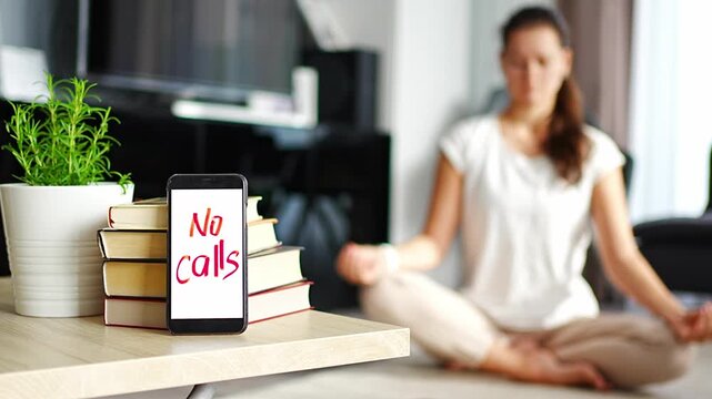 Digital detox concept. In the foreground is a smartphone with the text No Calls and woman meditating in the background
