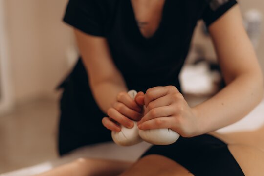 Therapist hands massaging client with hot herbal poultice