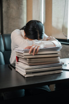 Tired employee resting head on a pile of paperwork at a desk, illustrating workplace fatigue and stress.
