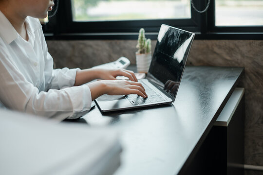 A woman in a white shirt working on a laptop at a modern desk with natural light and minimalist decor.