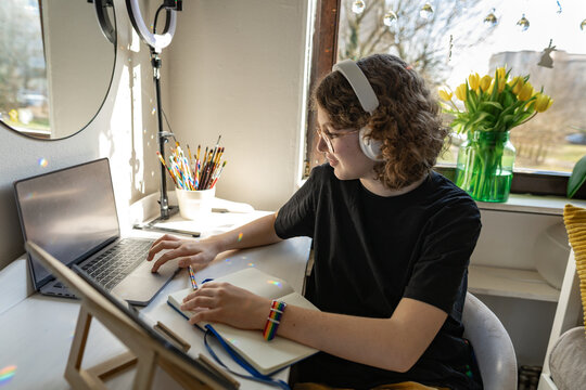 Creative youth with headphones sketching at cozy bedroom desk