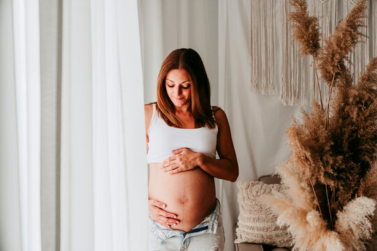 Pregnant woman at home gently touching belly in natural light